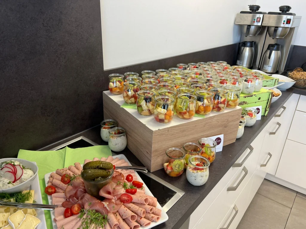 Verschieden Wurst- und Käseplatten, daneben Obstsalat in kleinen Gläsern